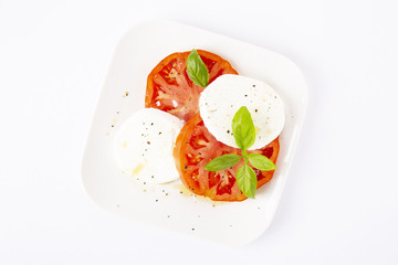 Mozzarella and tomatoes with basil on a white square plate. The background is white. Copiespice.