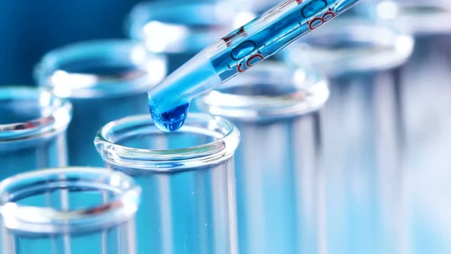 Liquid in a pipette with measured numbers drips into test tubes. Close up.