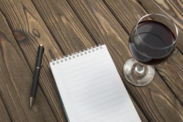 a notebook on a spiral, a ballpoint pen, a glass of red wine on a wooden table background. inspiration, intelligent thoughts.