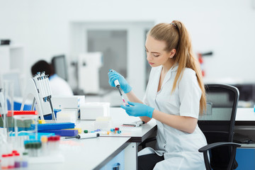 Pipette dropping a sample in a test tube. Laboratory assistant analyzing blood in lab. DNA analysis