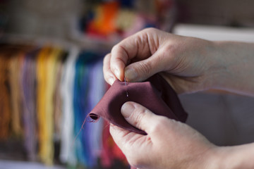 A man sews a cloth with a needle on a background of thread and cloth