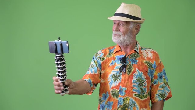 Handsome senior bearded tourist man ready for vacation against green background
