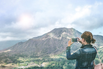 Fototapeta na wymiar Successful woman hiker taking picture with smartphone at cliff edge on mountain top. Bali island.