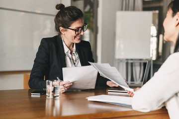 Photo of successful woman holding resume and negotiating with female candidate during corporate...