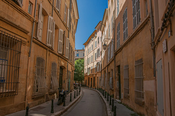 Narrow alley with tall buildings in the shadow in Aix-en-Provence, a pleasant and lively town in the French countryside. Located in Bouches-du-Rhone department, Provence region, southeastern France