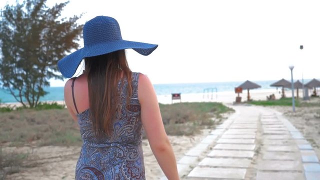 Young girl in a blue hat and glasses goes to the sea. Slow Motion