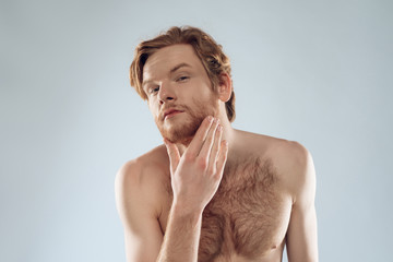Red haired young man is stroking beard.