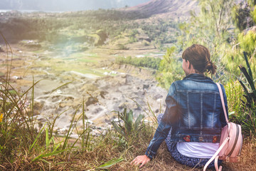 Young woman sitting on a rock with backpack and looking to the horizon. Bali island. Volcano Batur.