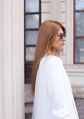 A woman in a white jacket and sunglasses looks away from the column. Street style. Fashion