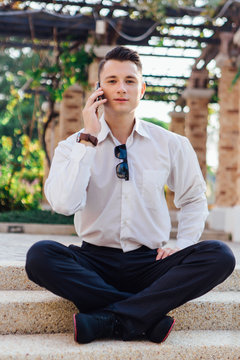 Young businessman sitting and talking on his phone outdoors