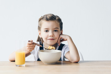 smiling little schoolgirl eating healthy breakfast isolated on white