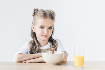 confident little schoolgirl sitting at table with breakfast isolated on white