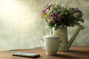 Obraz na płótnie Canvas Flower bouquet in white water can, white coffee cup and smartphone place on wood desk with Polished cement wall.Retro design image.