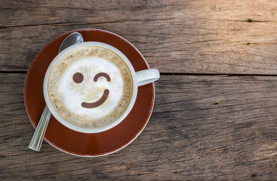 Top View Of Coffee Cup With White Foam And Smile Emotion Face On Wood Texture Background