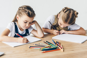 concentrated little schoolgirls drawing with colorful pencils in albums together isolated on white