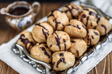 Profiteroles is a delicious culinary dishes of French cuisine with chocolate icing and nuts. Delicious profiteroles dessert on plate on dark wooden background.