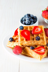 Photo of fresh homemade food made of berry Belgian waffles with honey, chocolate, strawberry, blueberry, maple syrup and cream. Healthy dessert breakfast concept with juice. 