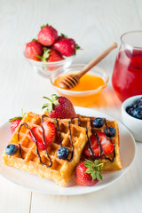 Photo of fresh homemade food made of berry Belgian waffles with honey, chocolate, strawberry, blueberry, maple syrup and cream. Healthy dessert breakfast concept with juice. 