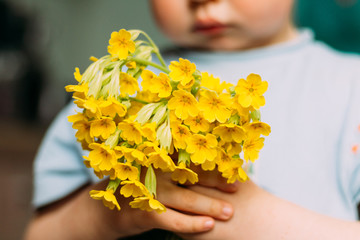 blur. The boy is holding yellow field flowers. gives them - showing in the camera. a gift to mom. to give a bouquet. gift - blurry bouquet of flowers