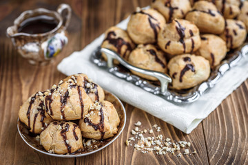 Profiteroles is a delicious culinary dishes of French cuisine with chocolate icing and nuts. Delicious profiteroles dessert on plate on dark wooden background.