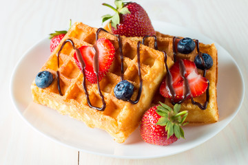 Photo of fresh homemade food made of berry Belgian waffles with honey, chocolate, strawberry, blueberry, maple syrup and cream. Healthy dessert breakfast concept with juice. 