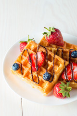 Photo of fresh homemade food made of berry Belgian waffles with honey, chocolate, strawberry, blueberry, maple syrup and cream. Healthy dessert breakfast concept with juice. 