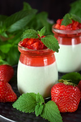 Two layered panna cotta with matcha tea topped with strawberry jelly, berries and mint in glass jars