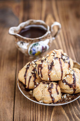 Profiteroles is a delicious culinary dishes of French cuisine with chocolate icing and nuts. Delicious profiteroles dessert on plate on dark wooden background.