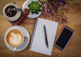 smartphone, diary, Flower, and coffee mug on wooden table.