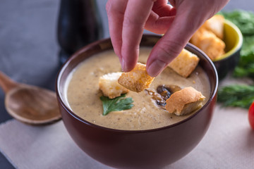 Female hand throwing crackers in cream of mushroom soup. Cooking of autumn vegetarian traditional dish