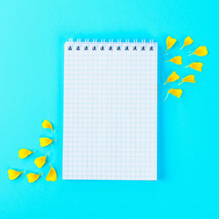 White empty notebook and yellow flower petals on a pastel blue background.