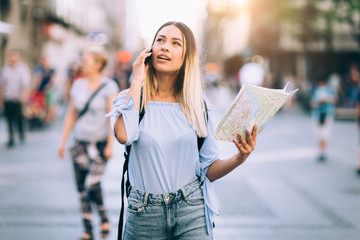Young beautiful female traveler lost in the city using map and mobile phone
