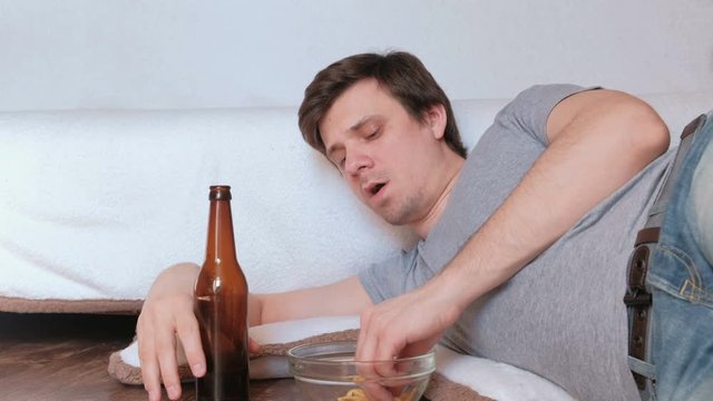 Handsome young man bachelor eating chips and drinking beer and watching TV.
