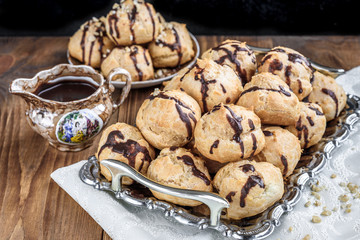 Profiteroles is a delicious culinary dishes of French cuisine with chocolate icing and nuts. Delicious profiteroles dessert on plate on dark wooden background.
