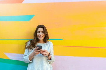 Outdoor portrait of hipster woman using a smart phone against colorful street wall