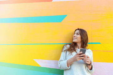 Outdoor portrait of hipster woman using a smart phone against colorful street wall