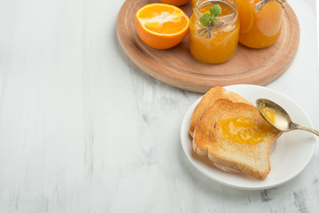 Orange jam in a glass jar on a light background with toasts. With empty space for writing