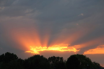 Wolkendecke bricht auf und zeigt die unterrgehende Sonne über dem Wald