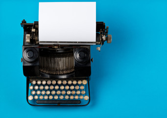Vintage typewriter top down flatlay shot from above with empty, blank sheet of paper on cyan