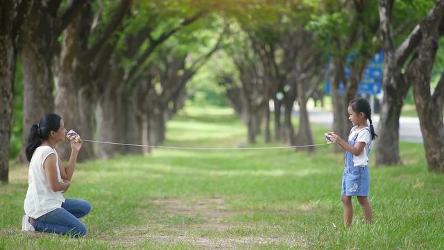 Slow motion, Asian family, mother and daughter doing string phone play activities tie rope at the park.