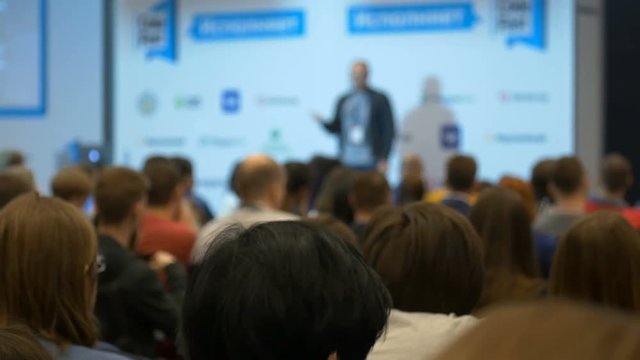 Blurred professional confident manager speaking at symposium for the public of male female persons, answering for colleagues from the big finance companies, giving advices, showing concept at chart