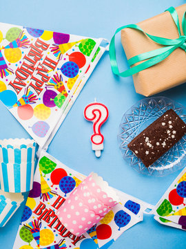 Happy Birthday party items flat lay. Gift box, decoration banner, paper glasses, chocolate cake. Question mark candle