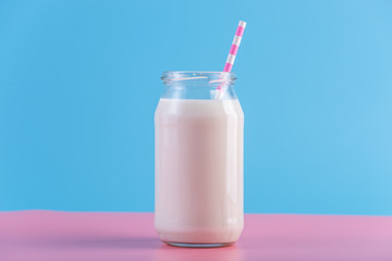 Glass bottle of fresh milk with straw on pastel background. Colorful minimalism. Healthy dairy products with calcium