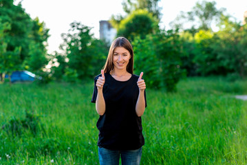 A happy young European girl. In the summer in park on vacation. Shows hand gesture two fingers up. A happy endorsement of emotion. Casual wear T-shirt jeans. Smiles on the teeth braces.