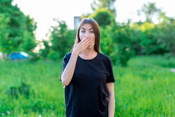 Beautiful brunette asian girl. In summer in the park in the fresh air. The gesture covers his mouth with his hands. Emotional surprise. Dressed in casual clothes.