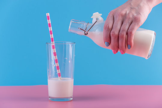 Woman's hand pours fresh milk from bottle into a glass on a pastel background. Healthy dairy products