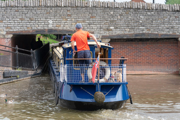 blue and cream canal boat being driven through small gap in tunnel under bridge in a tight fit