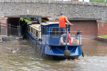 blue and cream canal boat being driven through small gap in tunnel under bridge in a tight fit