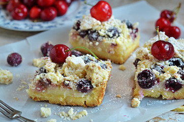 Square pieces of cake with cherries and crumble on paper