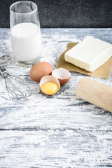 Bakery ingredients - flour, eggs, butter, milk, sugar on grey wooden table. Homemade bakery cooking.